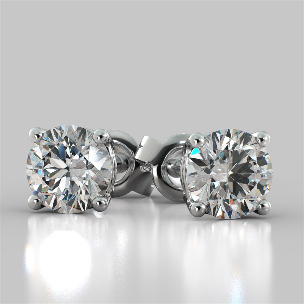 Diamond stud earrings on a reflective surface with a light gray background
