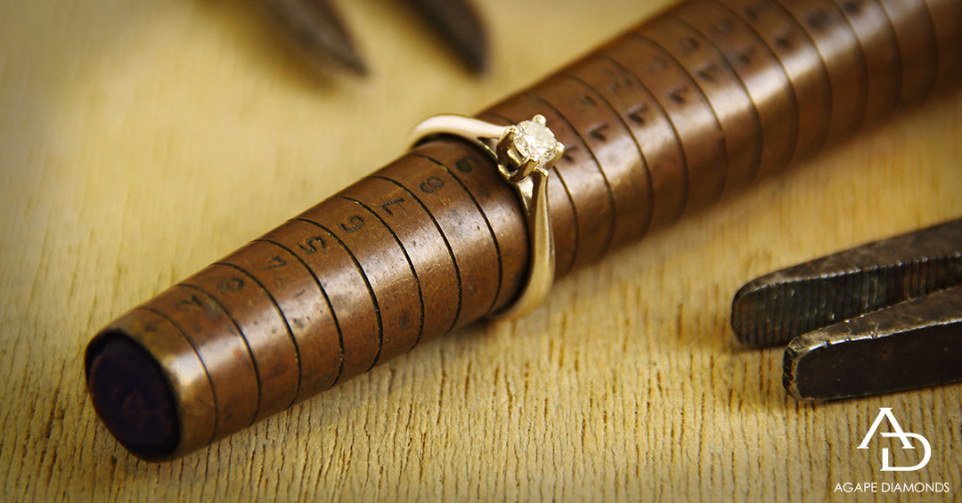 Gold ring on a wooden ruler with Agape Diamonds logo.