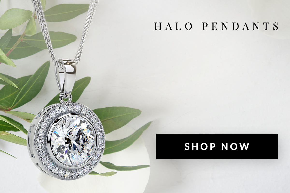 Silver halo pendant with a clear gemstone on a white background with green leaves.