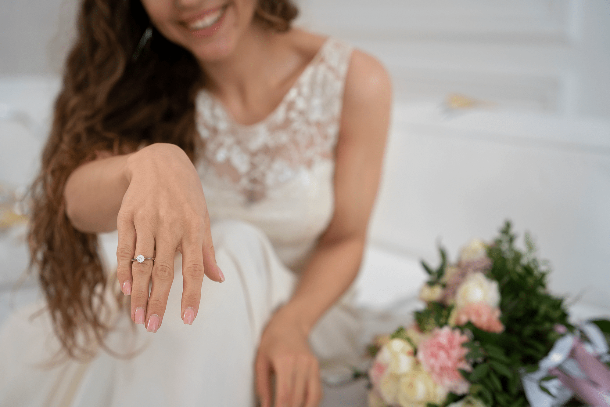 Woman in a wedding dress showing off a ring, with flowers in the background